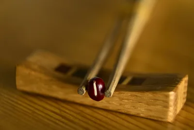 Red Gemstone Held By Tweezers Over Wooden Block - free art & design wallpaper 5728×3819