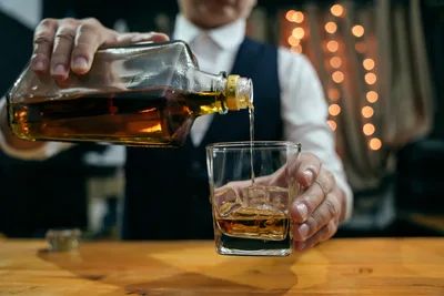 Man Pouring Whiskey Into Glass at Night - free food wallpaper 7008×4672