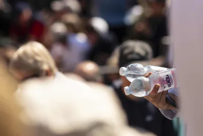 Hand Holding Water Bottles in Crowded Setting - free photography wallpaper 5120×3414