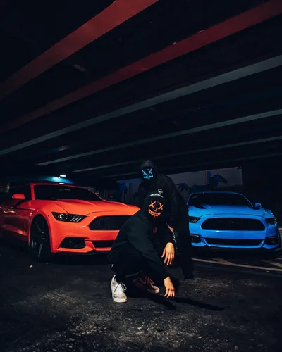 Neon Nights: Masked Figure Between Red and Blue Mustangs - free photography wallpaper 4430×5538