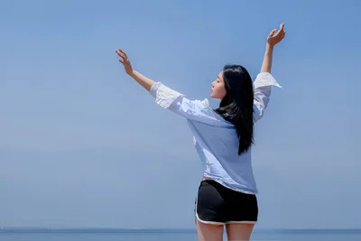 Woman Celebrating by the Sea with Arms Raised - free wallpaper 5120×3412